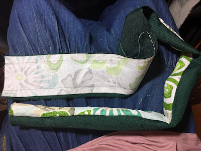 A half-turned tube of fabric, one side dark hunter green and the other a teal, white, and green tropical floral, on the denim-skirted photographer's lap.