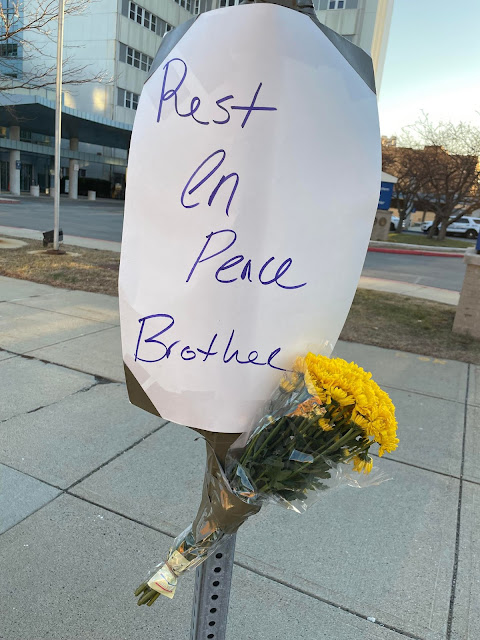 Posterboard with flowers taped on sign, words on sign: "Rest in Peace Brother"