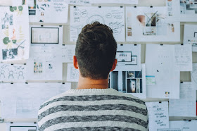 Young man looking up at lots of papers on wall, thinking, productivity, video game alternatives