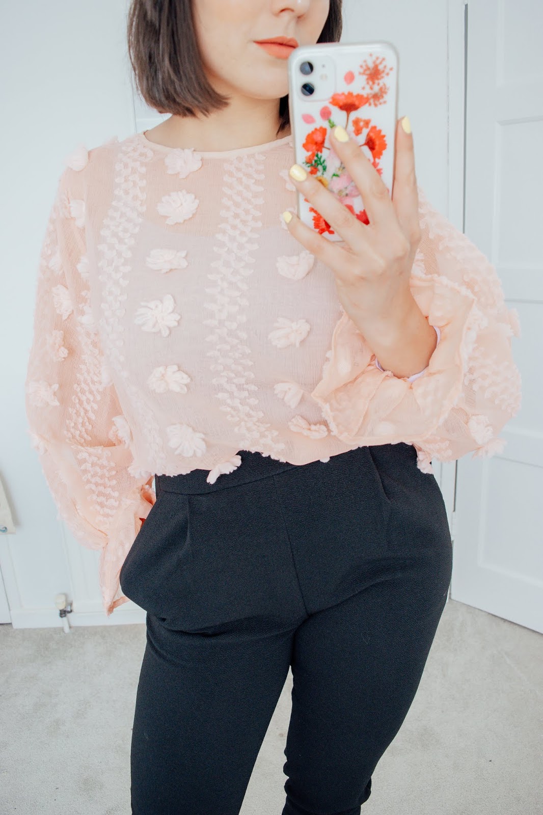 Person holding a phone wearing a pink blouse and black trousers.