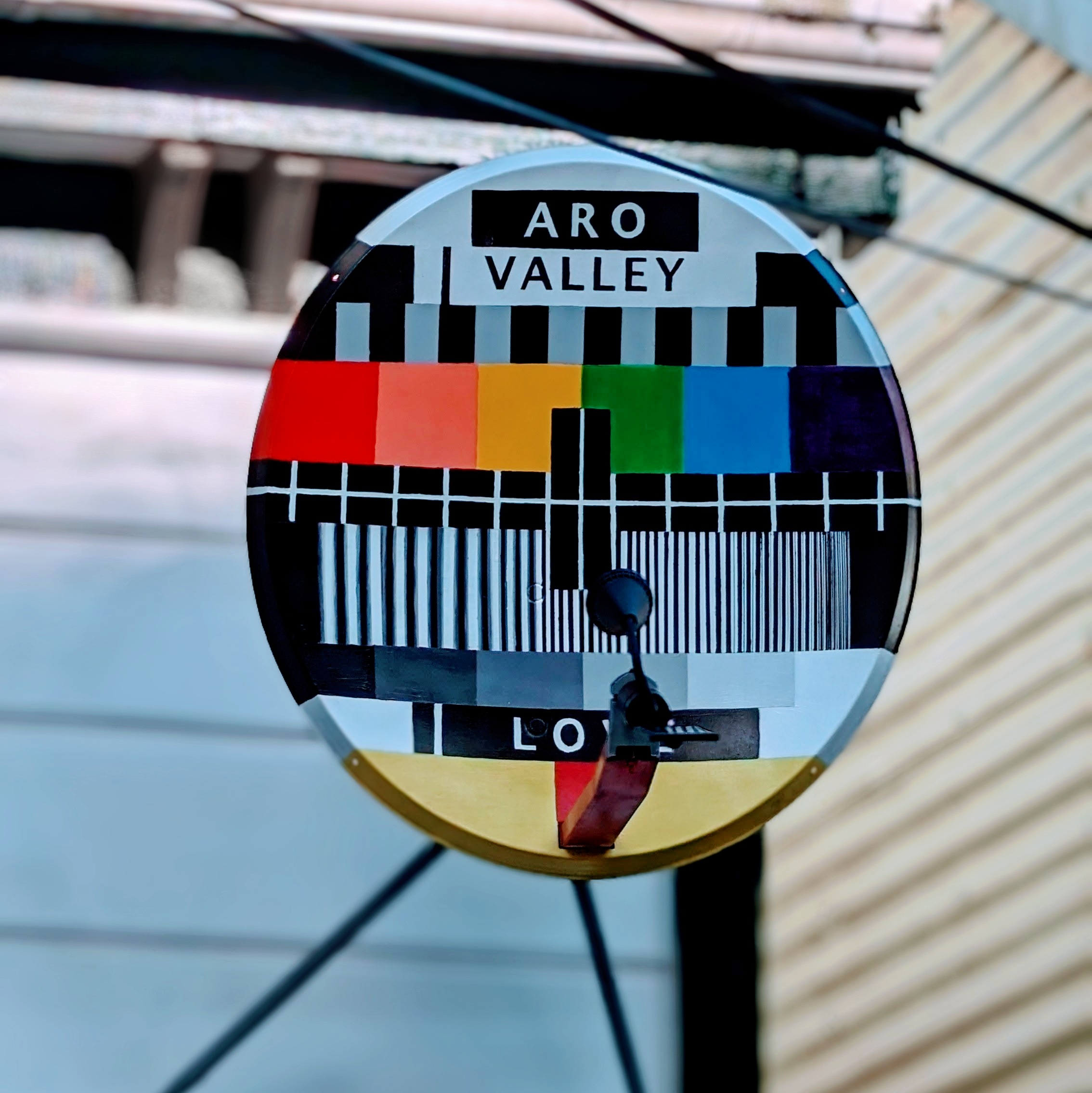 Satellite dish on the side of a house. The dish is painted with the 'Philips PM5544 Philips Television Test Pattern. The colours of the pattern were altered to represent those of the rainbow' with the words 'Aro Valley' on top and 'Love' on the bottom.