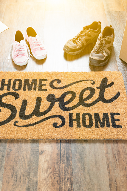 A cute welcome mat surrounded by shoes of the family.