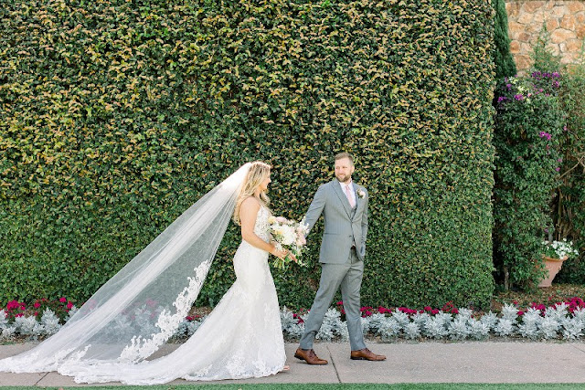bride and groom walking hand in hand in front of hedge wall