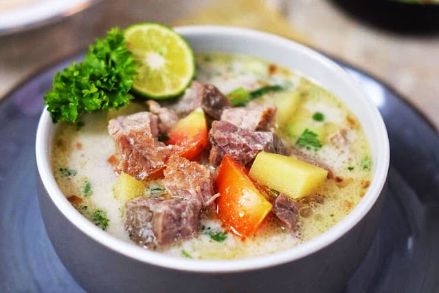 Traditional Soto Betawi soup served with beef, coconut milk broth, rice, emping crackers, and fresh herbs on the side