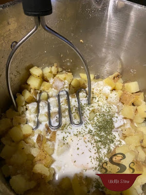 Cubed potatoes topped with buttermilk, seasonings, and a masher waiting to be used.