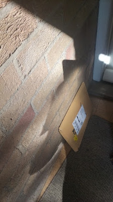 A brick porch wall with a cardboard parcel leaning against it