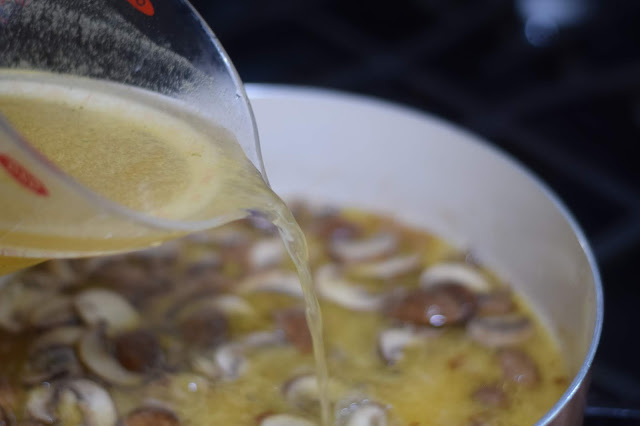 Chicken broth being added to the pan on the stove. 