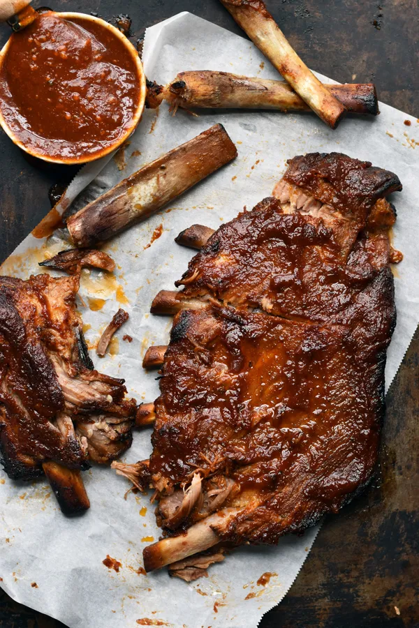 Juicy and tender St. Louis style slow cooker ribs, covered in savory BBQ sauce, plated on a baking sheet lined with parchment paper and ready to be devoured.