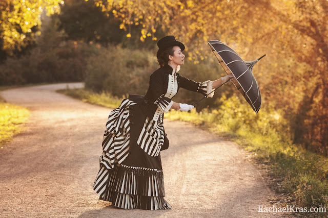 Woman wearing victorian black and white striped bustle skirt with bodice, pagoda umbrella, top hat, white gloves