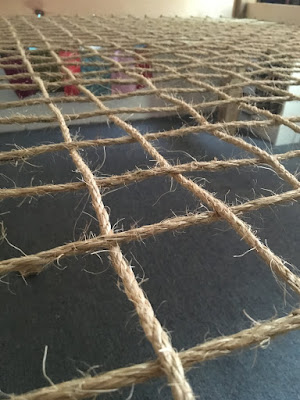 A low-angle photo of heavy jute rope woven in a grid, with a pale wooden bedframe showing at the top of the photo.