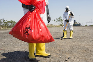 Men in protective suit pick up materials in biohazard bags.