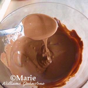 Melted chocolate in a glass bowl dripping off a spoon