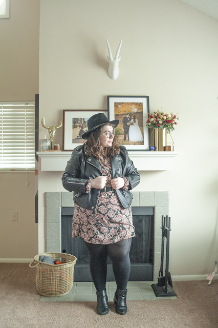 An outfit consisting of a black wide brim hat, a black faux leather moto jacket over a paisley peter pan collar shirt dress and black chelsea boots.