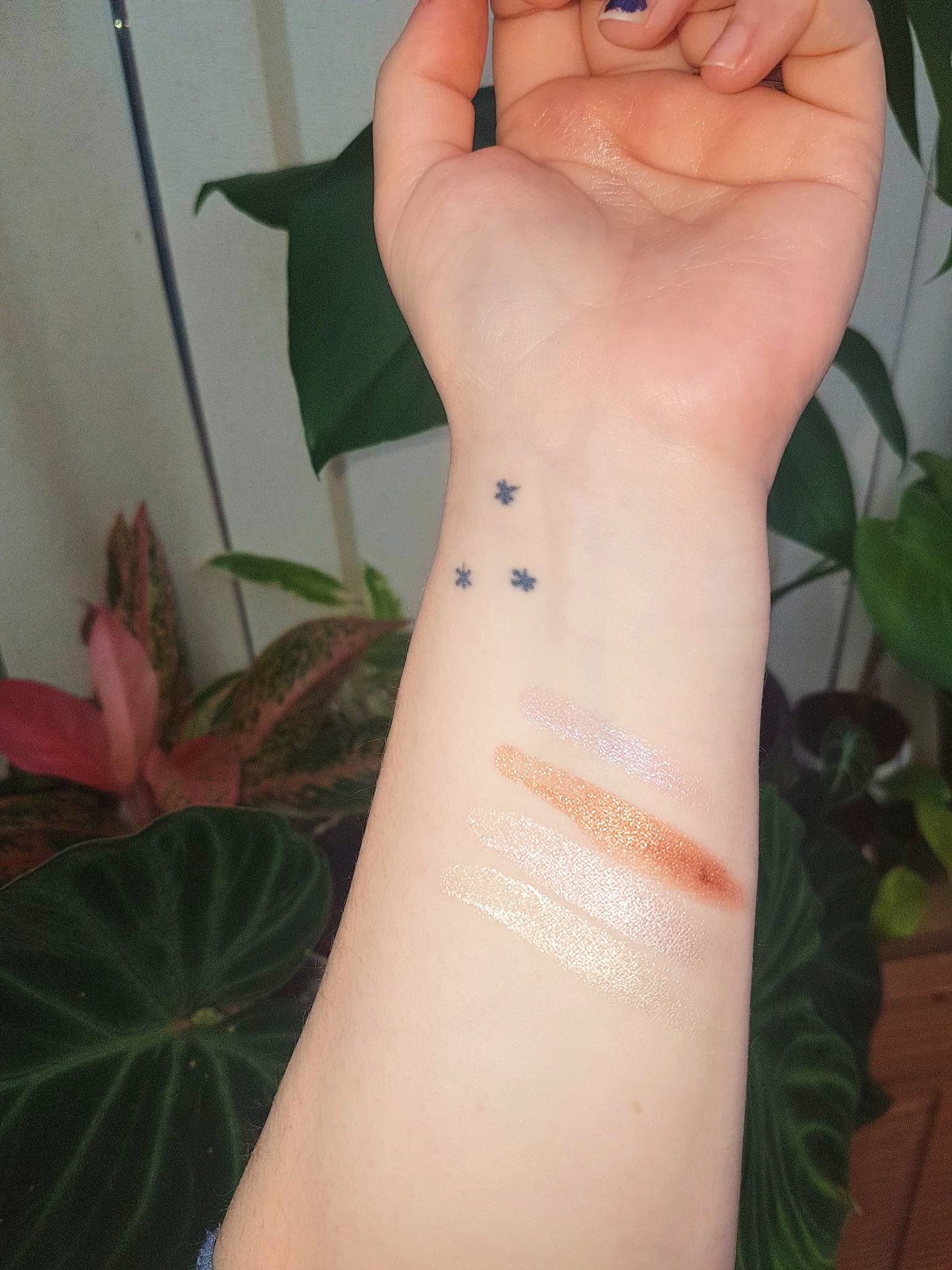 Madara Cosmic Drops Natural Liquid Highlighter Swatches on light skin tone arm with plants in the background