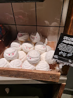 A photo of a light brown box filled with spherical white bombs that look like wrapped up mummy’s heads with red eyes with a rectangular black card with Jason’s mummy in white font on a bright background