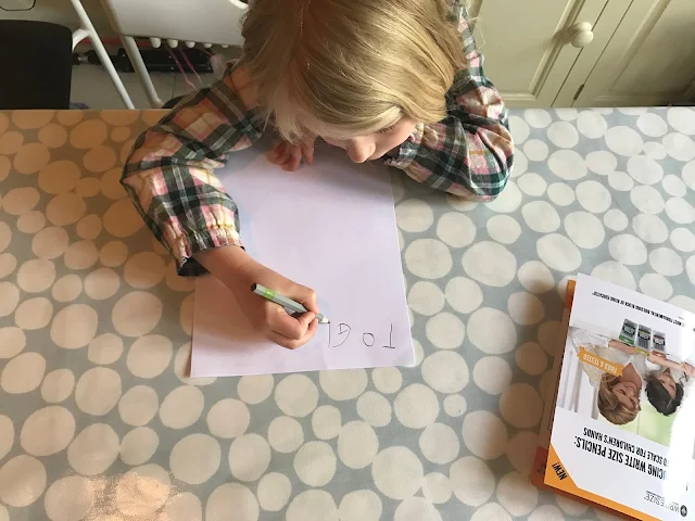 M is sitting at the table writing a letter. SO far she has written "To Gr"