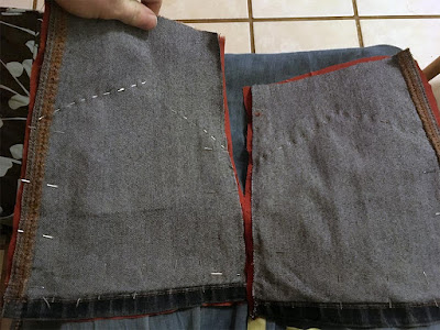 A pair of wrong-side-up pieces of hemmed denim, pinned to red fabric that just shows around the edges, with shallow points marked out by pins on each piece.