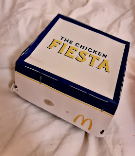 A square white box with the chicken fiesta in green font on a bright background