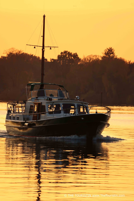 A boat at sunset, whereby the water, as well as the sky, is bathed in a deep orange colour.