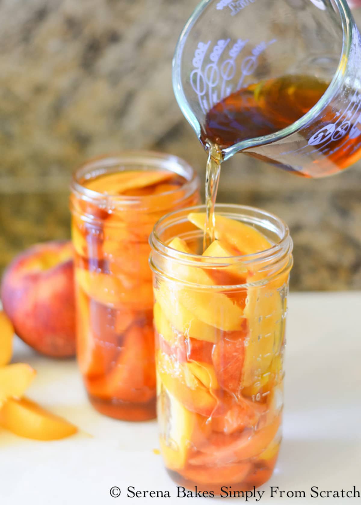 Whisky mixture being poured over peaches in a mason jar to cover.