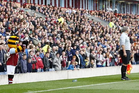 Burnley mascot Bertie Bee gestures that the assistant referee needs glasses