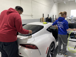 Two restyling workers apply car window tint in Livonia