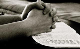 hands clasped in prayer resting on a Bible