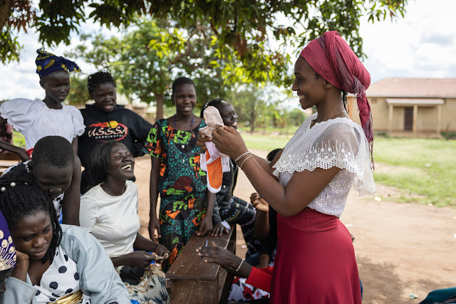 A smiling women holding up reusable sanitary towels in front of a group of women