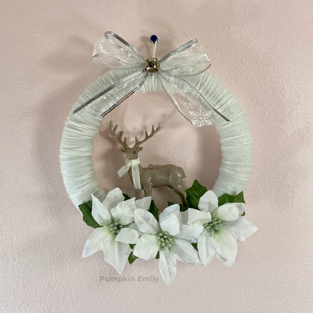 A winter yarn wreath with a deer, bow, and flowers.