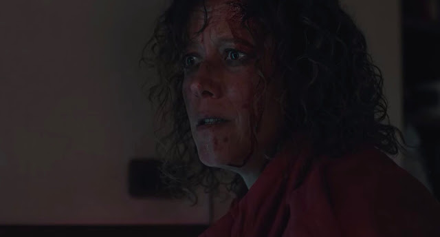 A woman stares wild-eyed. she has blood on her face