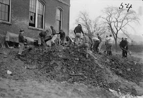 A black and white photograph of a group of men digging in dirt outside a building.