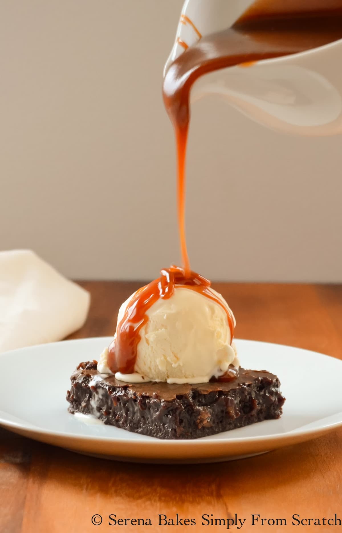 Homemade Caramel Sauce being drizzled over a chocolate brownie with a scoop of vanilla ice cream.