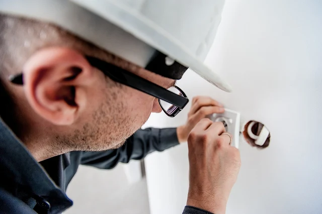 An electrician wearing a hard hat working on a plug socket