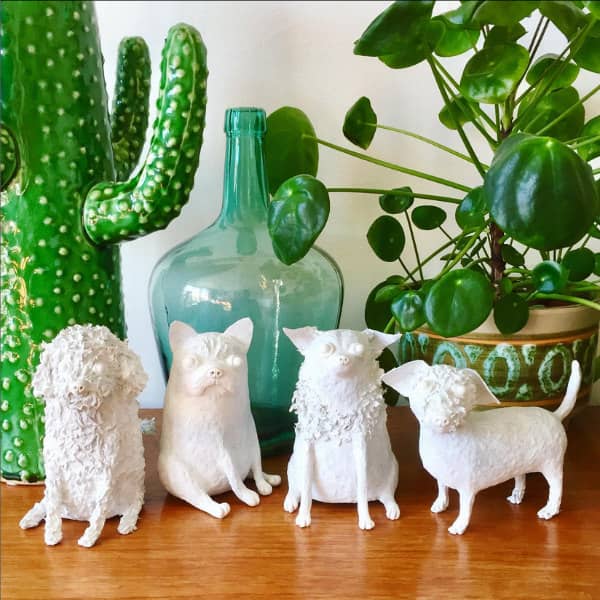 four unpainted paper mache dog sculptures on table placed in front of glass jar, green plant and paper mache cacti