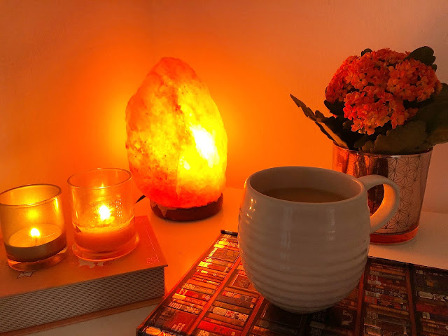 salt lamp next to two small candles and a cup of tea in white mug on top of notebook