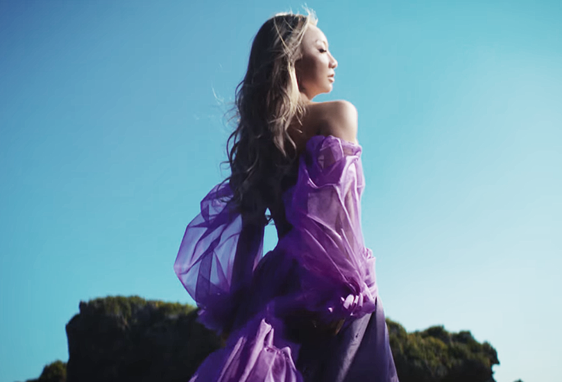 A screenshot of Koda Kumi in her music video for "Silence". Standing outside, wearing a purple dress made of (what looks like) silk and tulle.