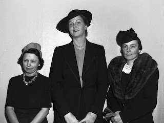 Junior League children's entertainment bureau meeting attendees (left to right) Miss Kathryn Waller, Miss Jo Kelly and Mrs. Bryant Nowlin are pictured here. The three women are shown standing side by side in a row against a bare wall and smiling for the camera. Miss Waller, Classroom Teachers Association, is wearing a short-sleeved dark dress with a jeweled necklace and a hair scarf. Miss Jo Kelly, Association for Childhood Education, is wearing a dark, long-sleeved jacket with a blouse underneath and a wide-brimmed hat. She has a brooch pinned to her blouse. Mrs. Bryant Nowlin, American Association of University Women, is wearing a coat that has a large, fur lapel and holding a pair of gloves. Published in the Fort Worth Star-Telegram morning edition, December 3, 1941.