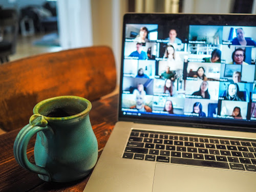 coffee cup in front of computer displaying a Zoom video conference meeting