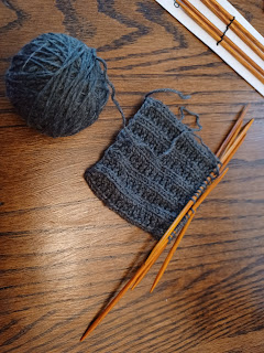 one small ball of grey yarn being knit slowly into a mitten; new set of needles just visible in the corner