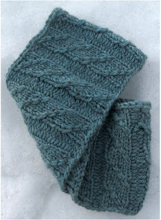 a cowl knit in light-blue worsted weight yarn, with a cable that crosses columns of knit stitches.
