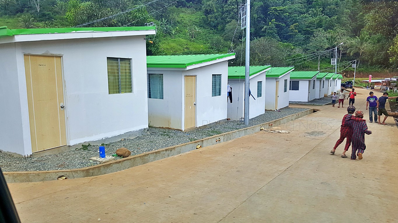 rows of newly built temporary shelters in uneven terrain