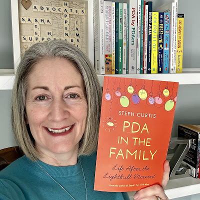 grey haired me smiling at camera holding up pda in the family book that has orange cover