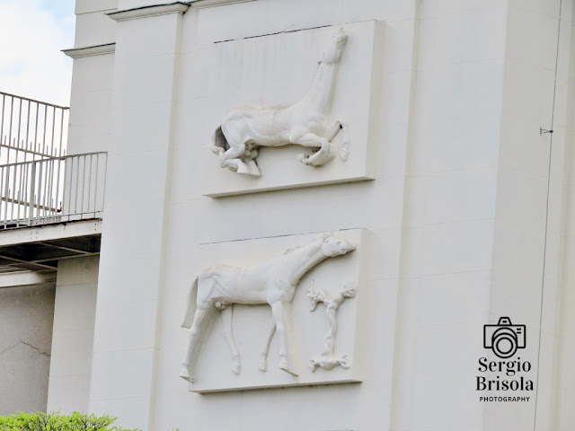 Vista ampla de dois painéis escultóricos em alto-relevo da fachada da Tribuna dos Sócios do Jockey Club