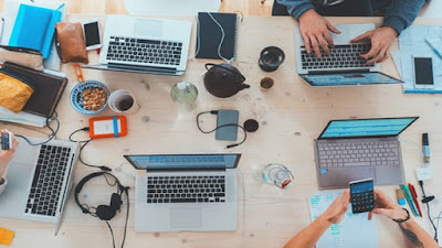 Internet business work station with computers, mobile phones, head phones, mugs of beverages and notepads.