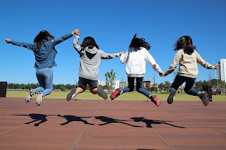 group of girls facing away from the camera, holding hands and jumping