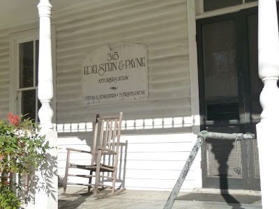 Personal Injury Law office exterior 315 E. Jones St. Raleigh, NC 27601, USA White painted shingles, columns, flowering bushes, black screen door wooden rocking chairs Sign Edelstein & Payne attorneys at Law Steven Edelstein M. Travis Payne