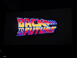A photo of the title screen of Back To the Feature on a screen at a drive in theater