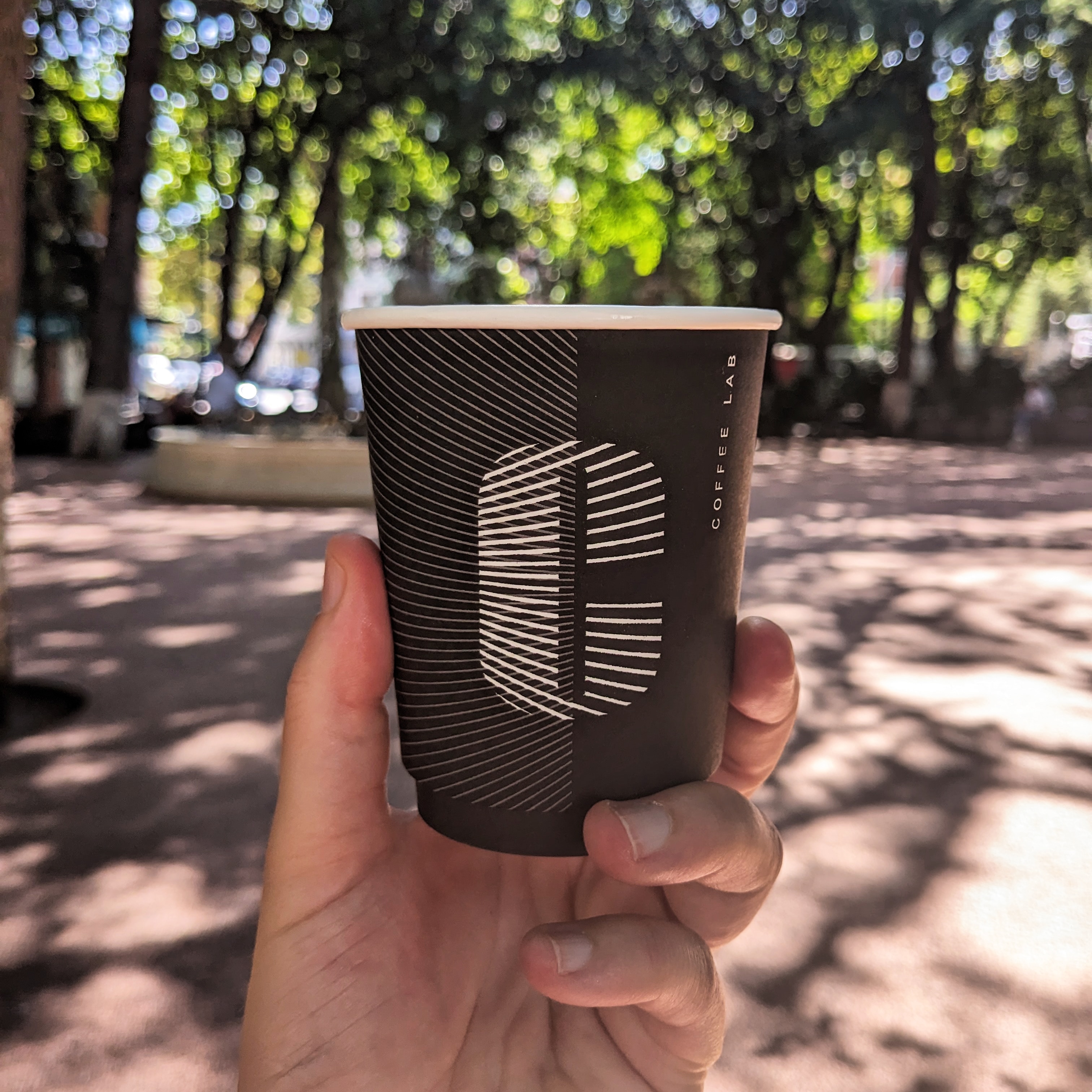 A flat white in a black take out coffee cup embellished with a white letter c. The coffee is from Coffee Lab, one of the best cafes in Tbilisi