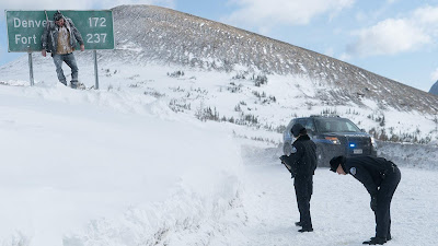 A dead body hangs from a road sign as Emmy Rossum and John Doman investigate in the new film "Cold Pursuit"