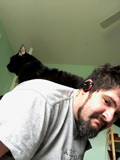 A large black cat on a white bearded man's back (again, me).